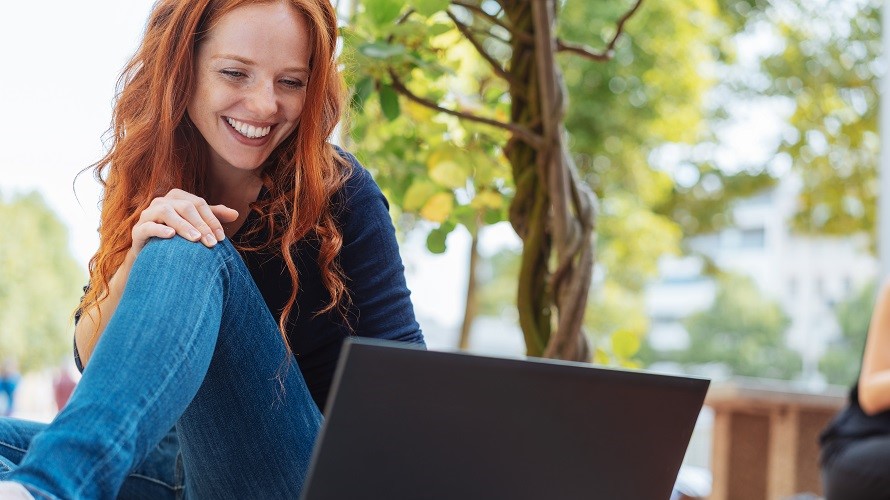 Frau mit Laptop im Freien Eine rothaarige Frau sitzt am Boden im Garten und arbeitet am Laptop.